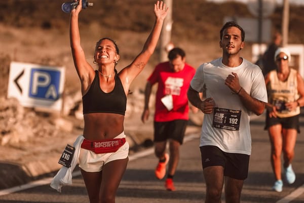 Woman throwing her hands up in joy as she runs an endurance road race alongside other courageous runners.